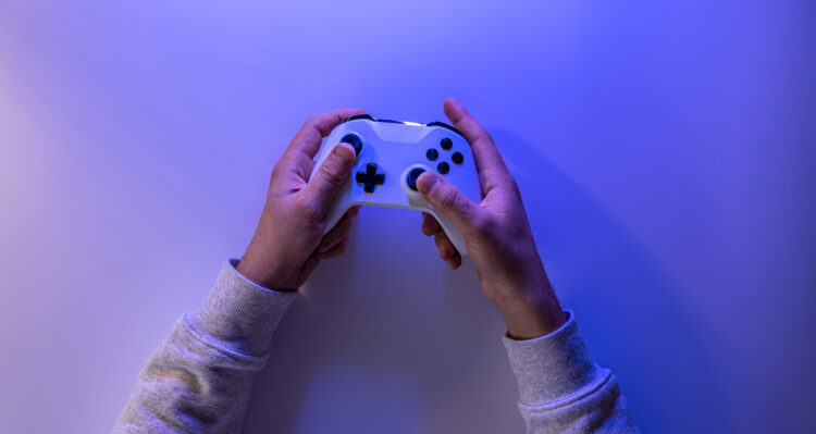 Male hands hold a gamepad on a blue background, copy space.