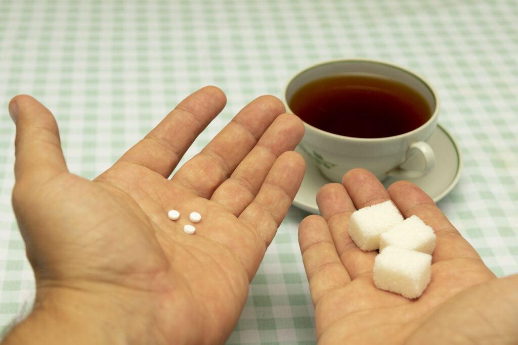 Three small sweetener tablets replacing three teaspoons of sugar in hand for adding to a cup of tea